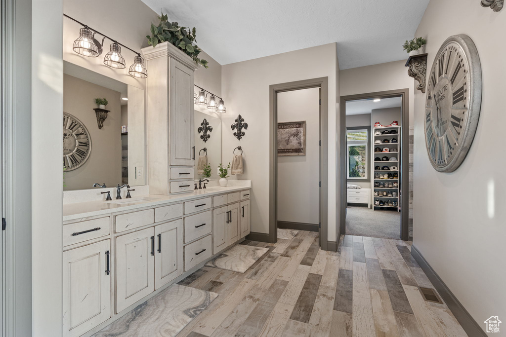 Bathroom with double vanity, baseboards, wood finished floors, and a walk in closet