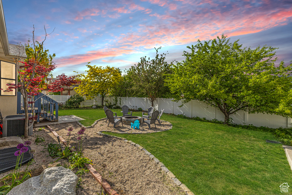 Yard at dusk with an outdoor fire pit, a fenced backyard, and a patio area