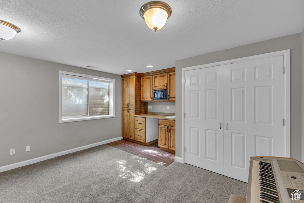 Kitchen with black microwave, light colored carpet, brown cabinets, baseboards, and recessed lighting
