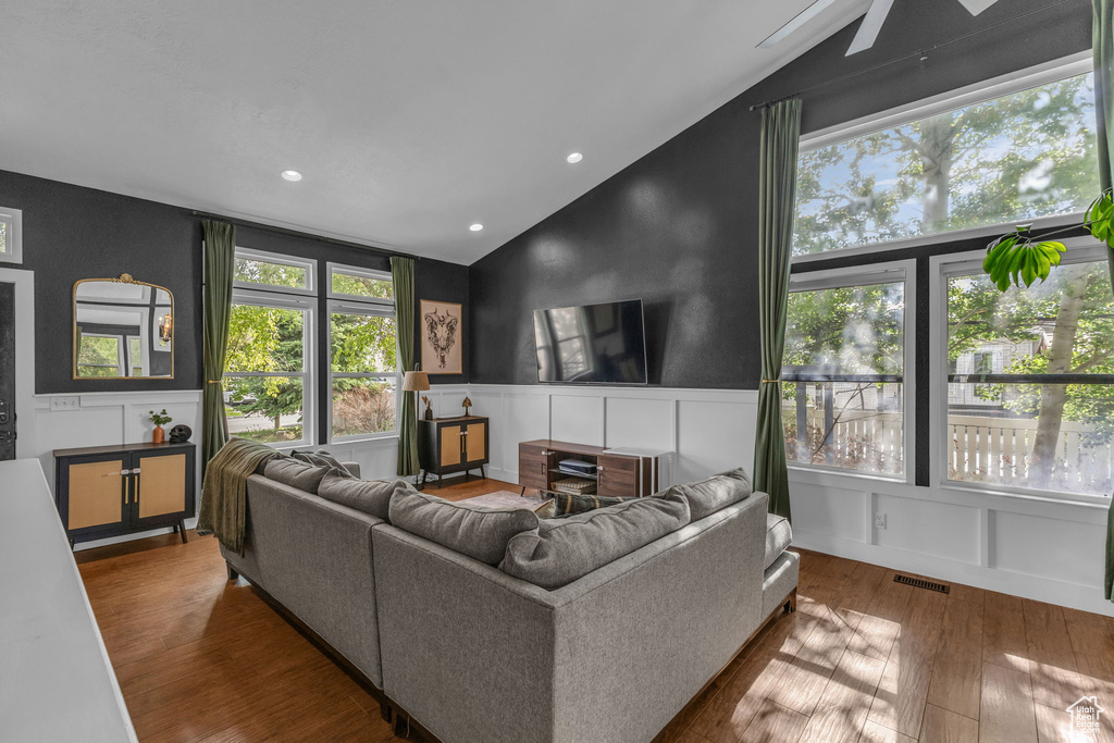 Living area featuring lofted ceiling, a decorative wall, wood finished floors, wainscoting, and a ceiling fan