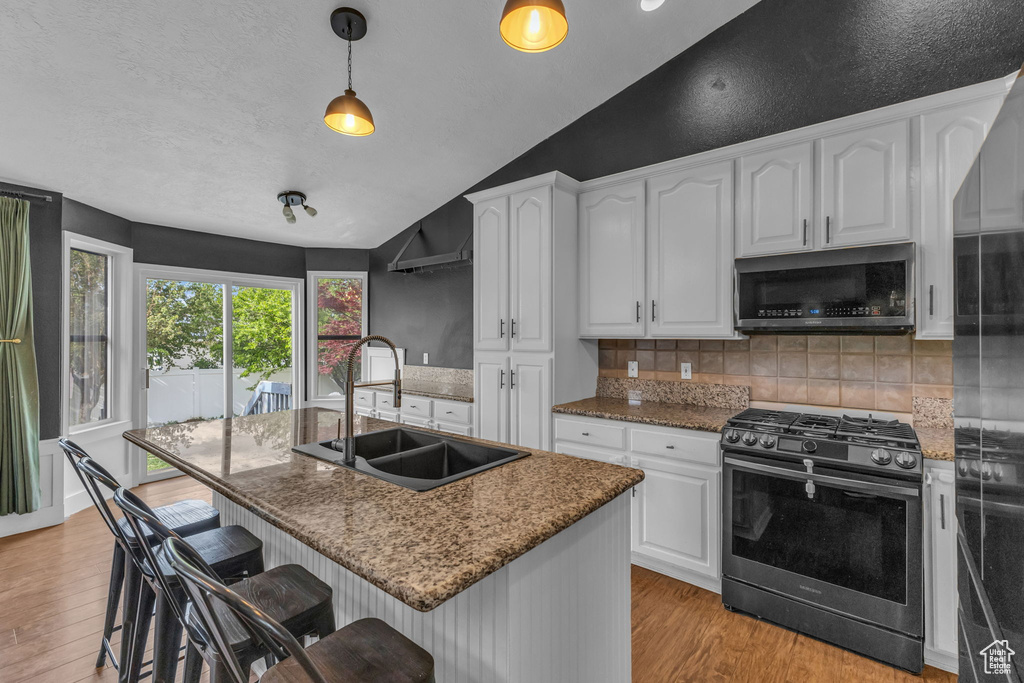 Kitchen featuring stainless steel appliances, a sink, vaulted ceiling, light wood-type flooring, and backsplash