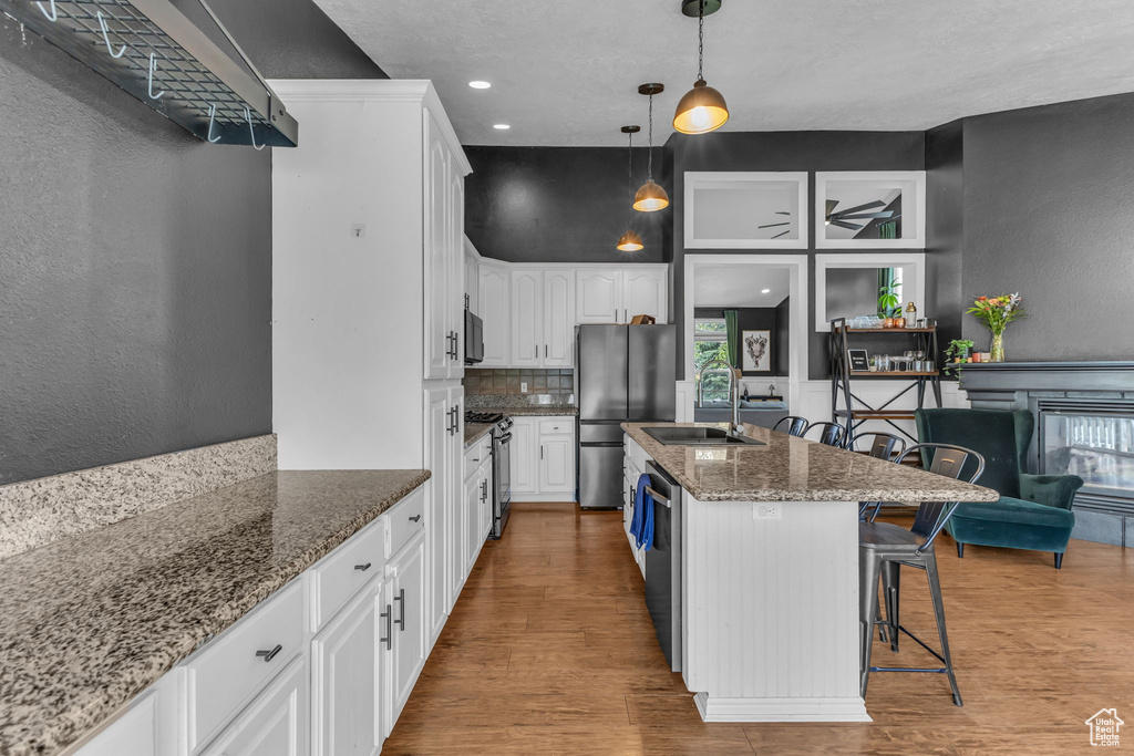 Kitchen featuring appliances with stainless steel finishes, a sink, white cabinets, wood finished floors, and dark stone counters
