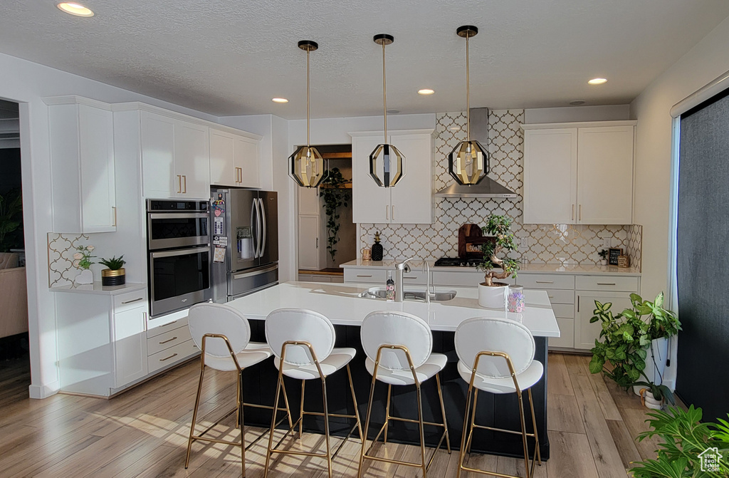 Kitchen featuring wall chimney exhaust hood, stainless steel appliances, light wood-type flooring, a breakfast bar area, and recessed lighting
