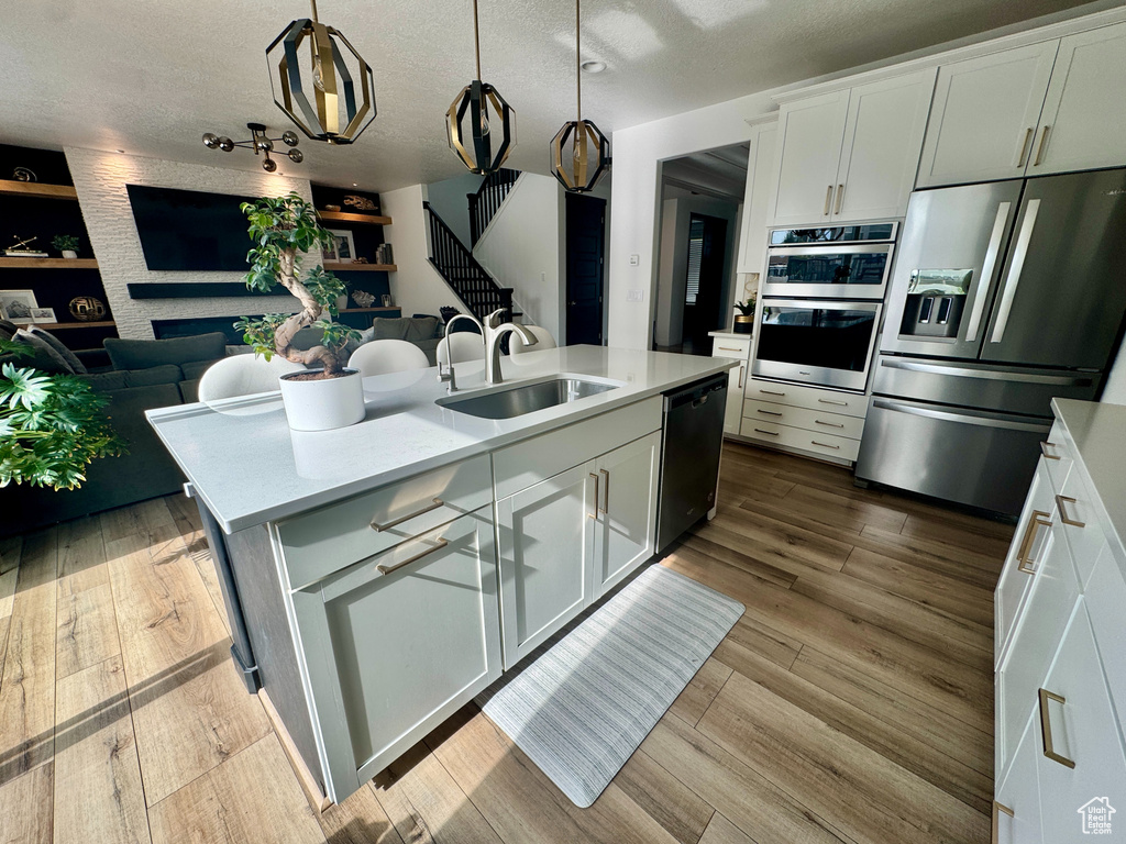 Kitchen featuring stainless steel appliances, a sink, open floor plan, light countertops, and white cabinets
