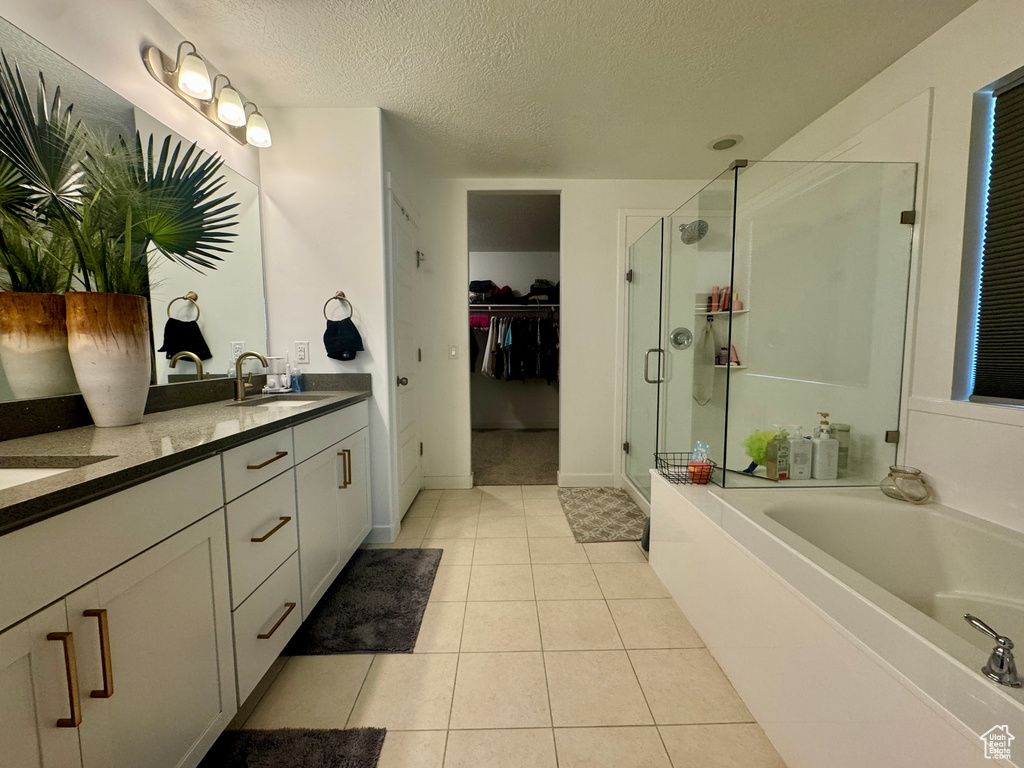 Full bath with a stall shower, a textured ceiling, double vanity, a spacious closet, and a bath