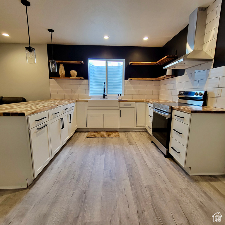 Kitchen with open shelves, stainless steel electric range oven, butcher block counters, a sink, and wall chimney exhaust hood