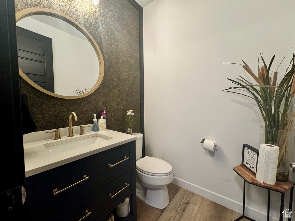 Half bathroom featuring wood finished floors, vanity, toilet, and baseboards