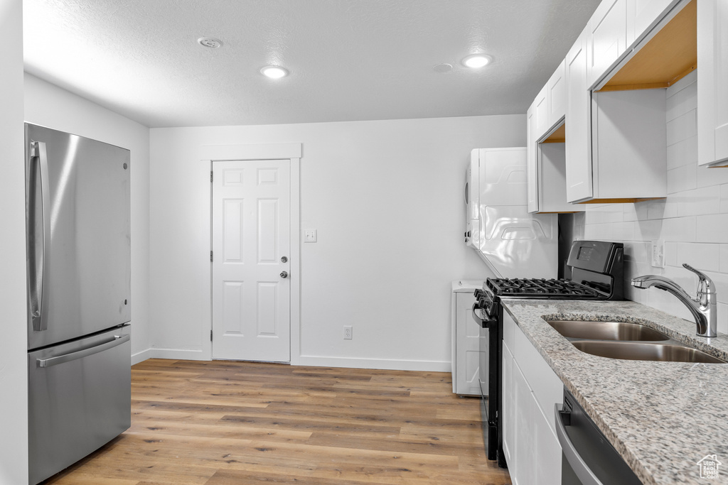 Kitchen with stainless steel appliances, a sink, white cabinets, decorative backsplash, and light wood-style floors