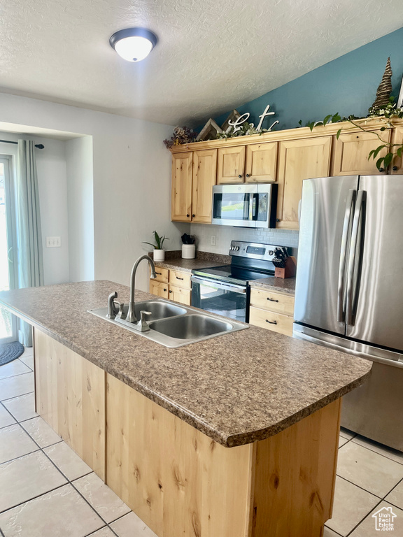 Kitchen featuring stainless steel appliances, light brown cabinetry, a sink, light tile patterned flooring, and a textured ceiling