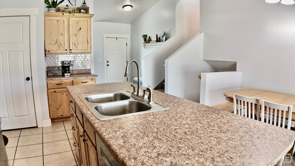 Kitchen with a sink, light tile patterned flooring, light brown cabinetry, tasteful backsplash, and light countertops
