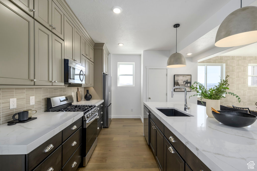 Kitchen with appliances with stainless steel finishes, a sink, baseboards, wood finished floors, and backsplash