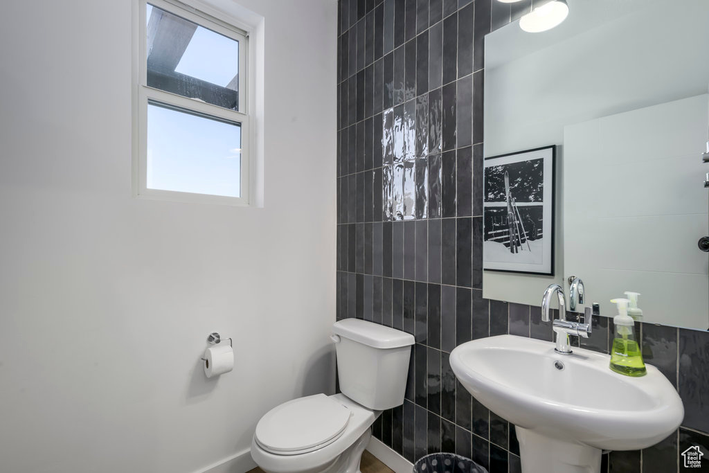 Half bathroom with plenty of natural light, toilet, tile walls, and a sink