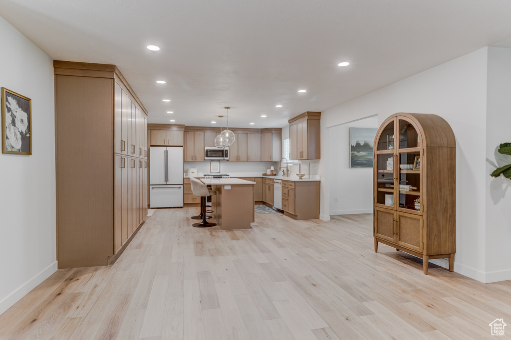 Kitchen featuring white appliances, a breakfast bar, light countertops, recessed lighting, and a kitchen island