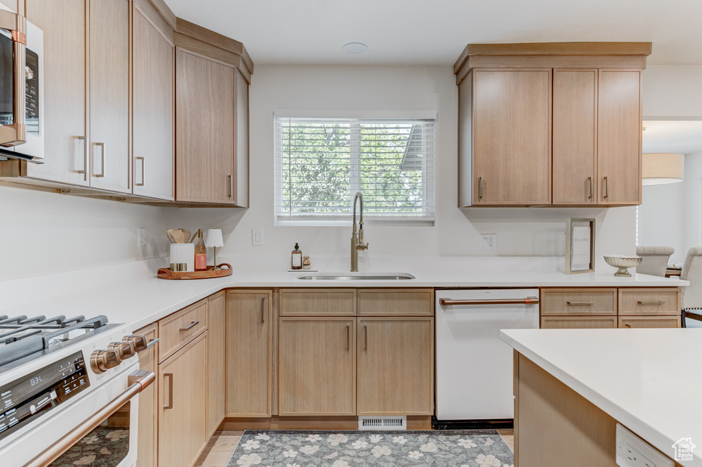 Kitchen featuring white appliances, light brown cabinets, a sink, and light countertops