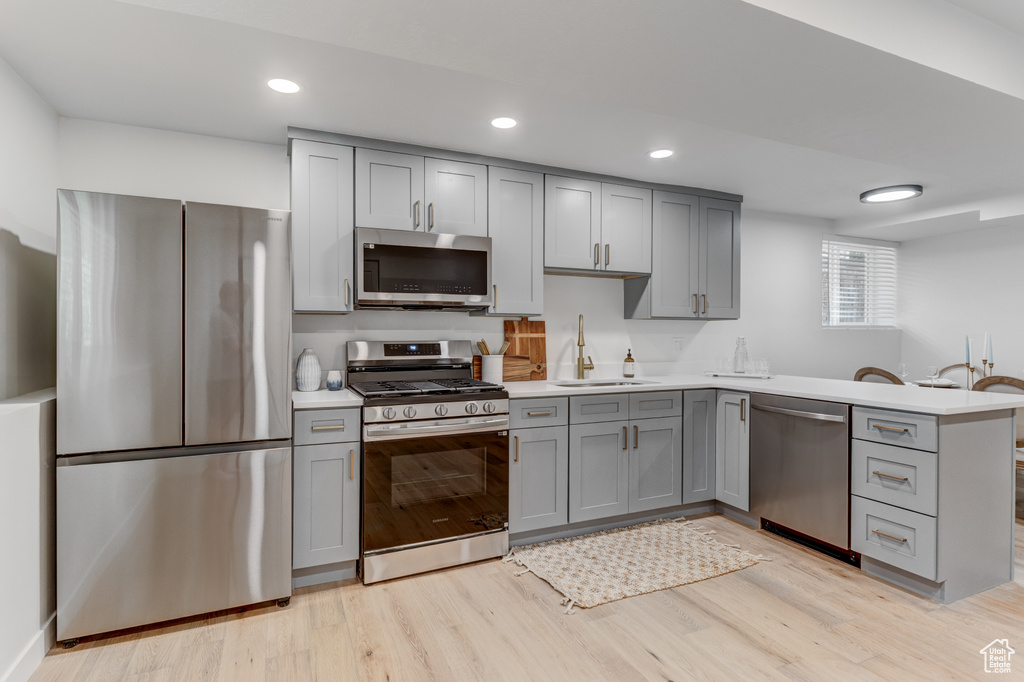 Kitchen featuring appliances with stainless steel finishes, gray cabinets, a sink, a peninsula, and recessed lighting