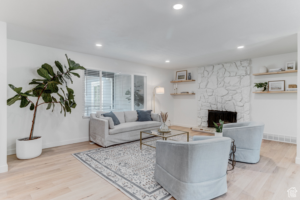 Living room featuring wood finished floors, a stone fireplace, baseboards, and recessed lighting