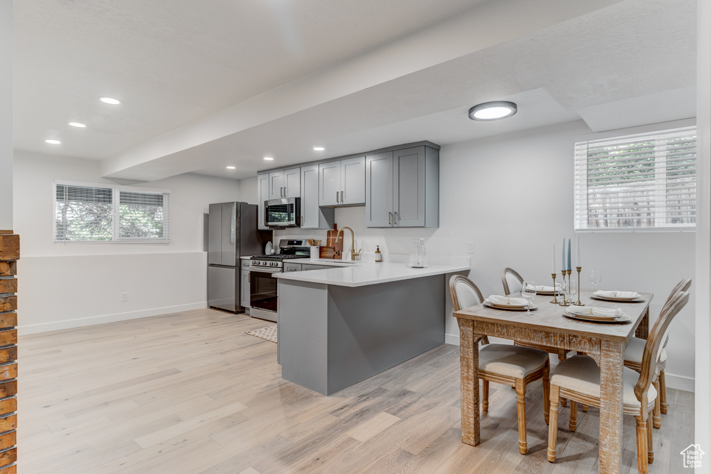 Kitchen with stainless steel appliances, light wood-style floors, gray cabinets, light countertops, and baseboards