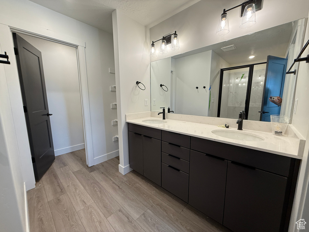 Full bath with a sink, double vanity, a shower stall, and wood finished floors