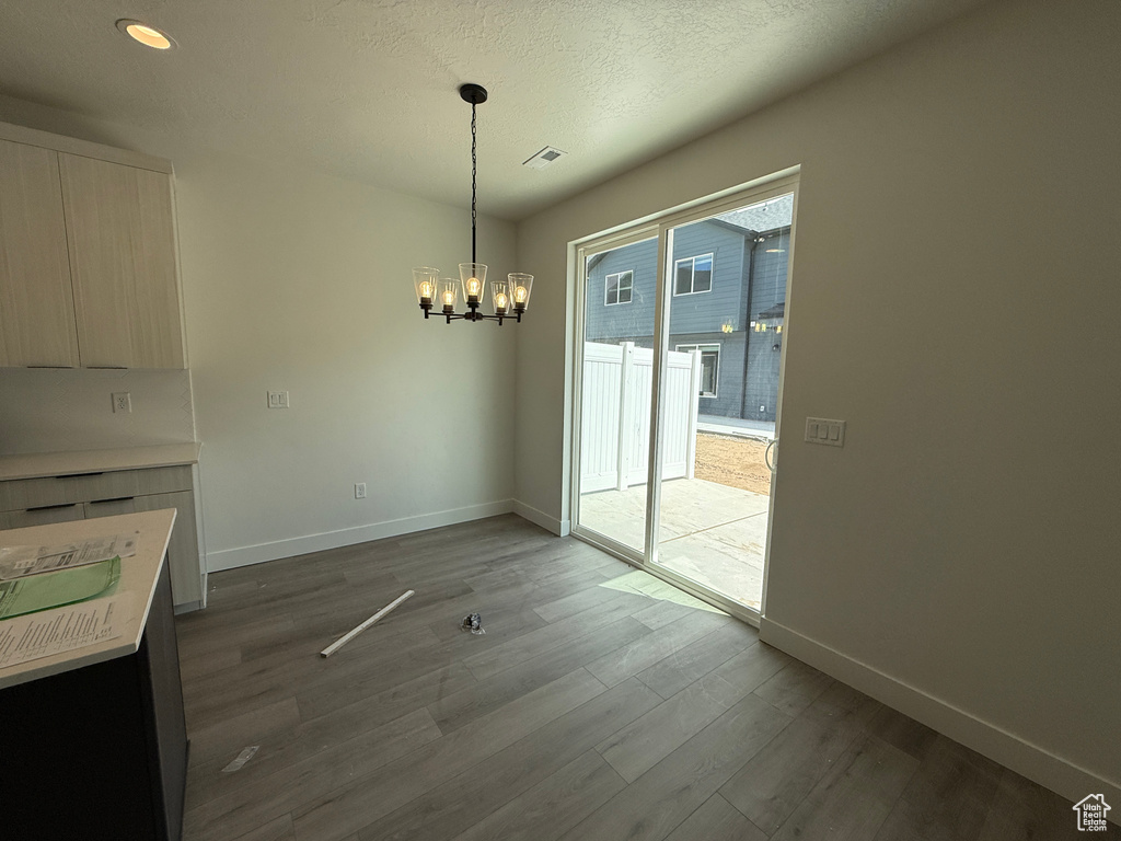 Unfurnished dining area featuring baseboards, visible vents, wood finished floors, and a notable chandelier