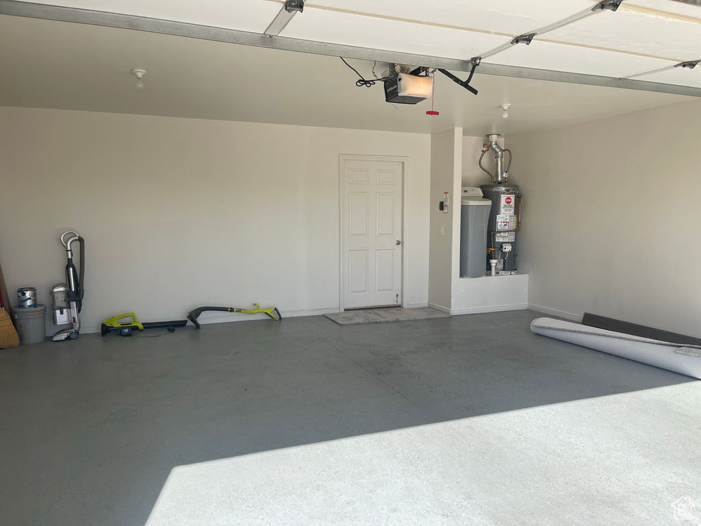 Garage featuring a garage door opener, gas water heater, and baseboards