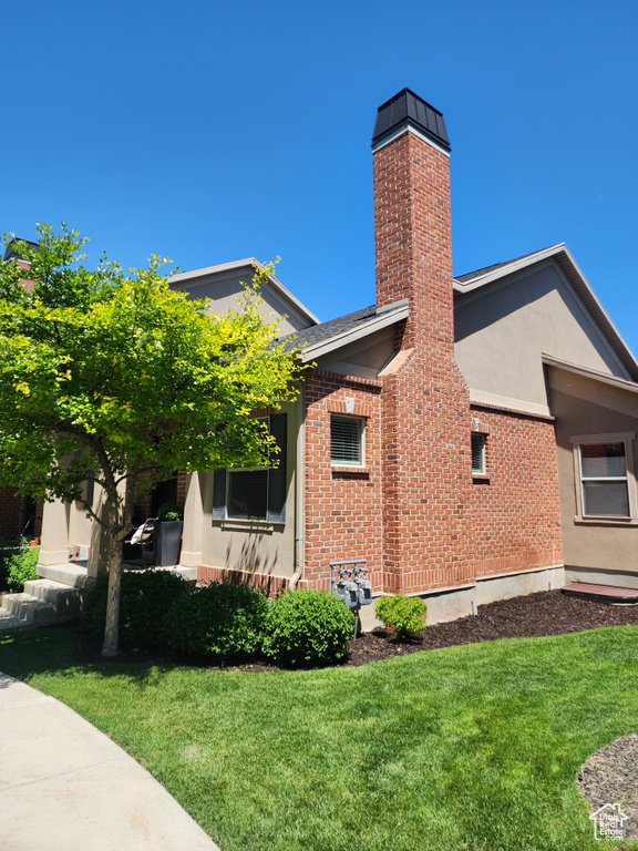 View of side of property featuring stucco siding, a lawn, a chimney, and brick siding