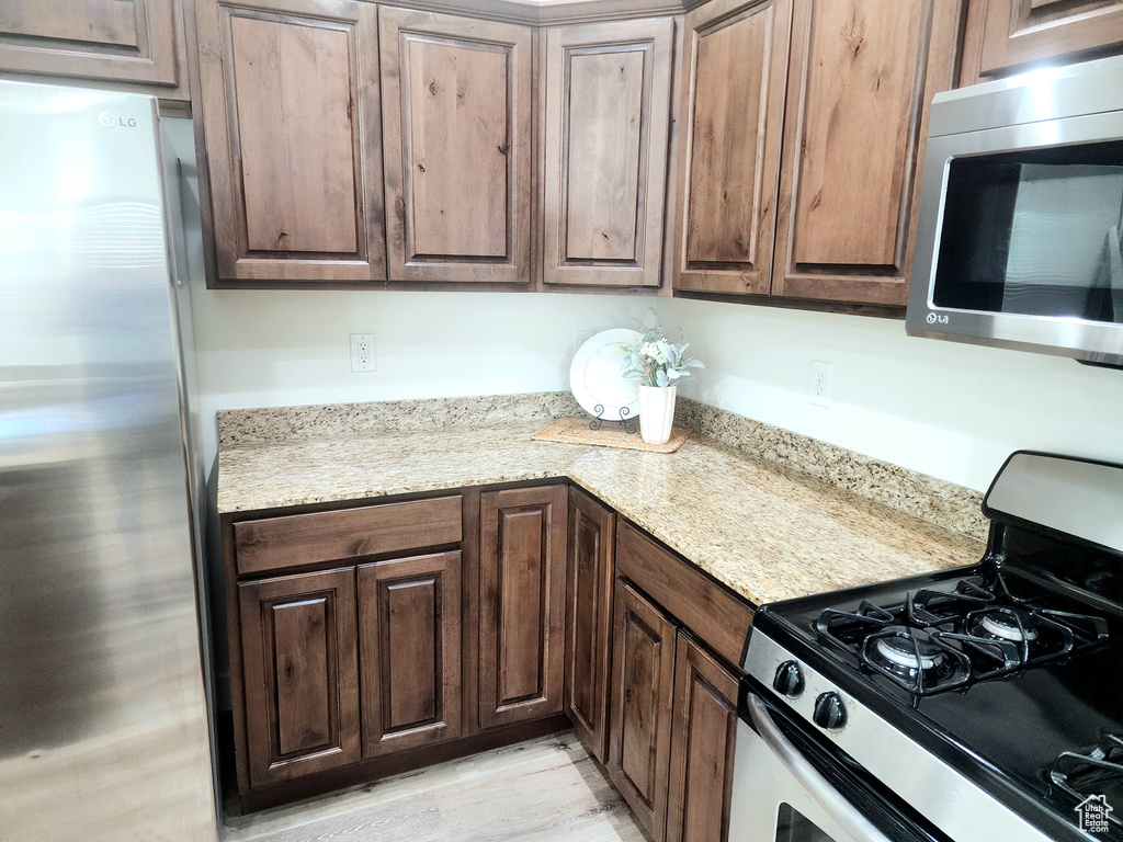 Kitchen with appliances with stainless steel finishes, light wood finished floors, and dark brown cabinets