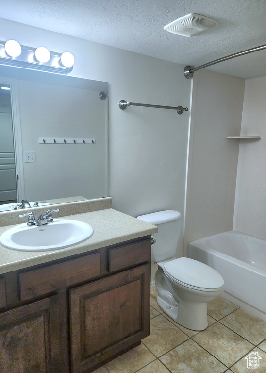 Full bath with vanity, a textured ceiling, toilet, tile patterned floors, and washtub / shower combination