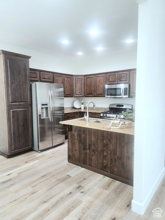 Kitchen featuring appliances with stainless steel finishes, dark brown cabinetry, light wood finished floors, light stone countertops, and recessed lighting