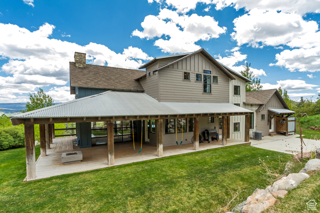 Rear view of property with board and batten siding, a patio, a lawn, and a chimney