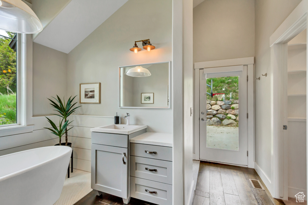 Bathroom with vanity, high vaulted ceiling, a soaking tub, and wood-type flooring