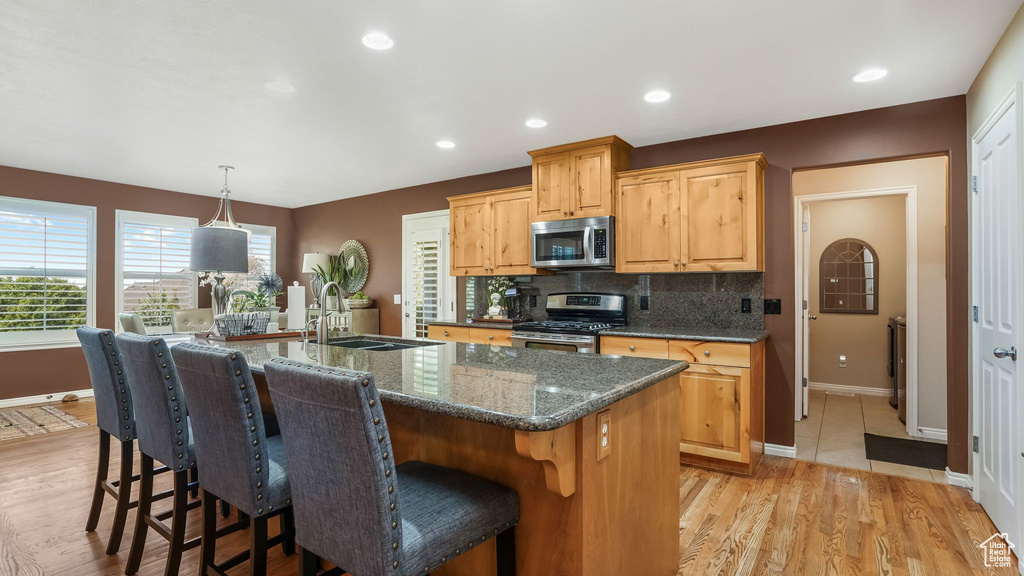Kitchen featuring stainless steel appliances, a sink, baseboards, a center island with sink, and tasteful backsplash