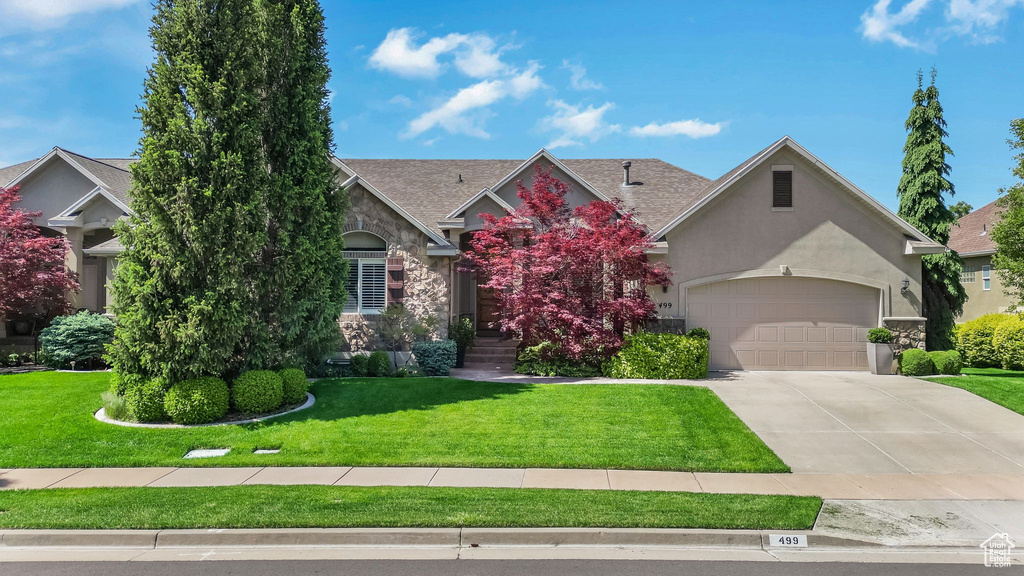 View of front of home with stucco siding, a front lawn, concrete driveway, stone siding, and an attached garage