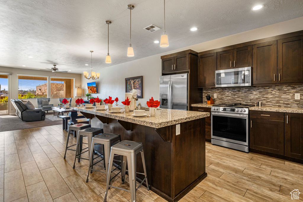 Kitchen with stainless steel appliances, open floor plan, light wood-style floors, dark brown cabinetry, and recessed lighting
