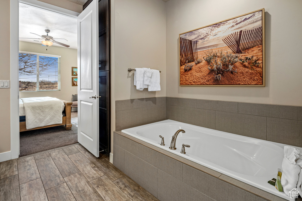 Bathroom with ensuite bathroom, wood finished floors, a bath, and a ceiling fan