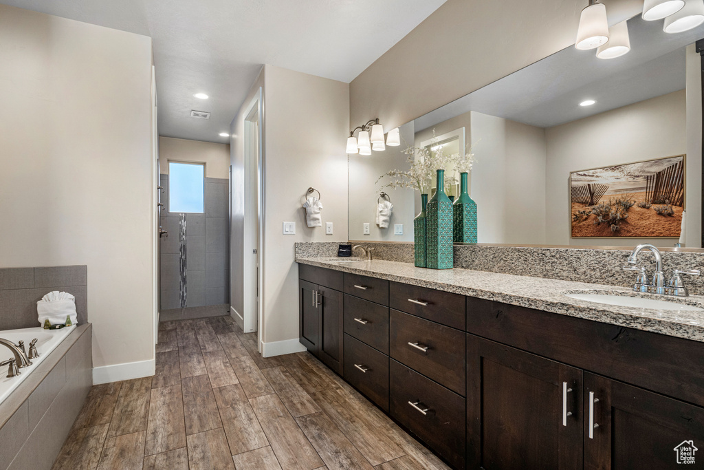 Full bathroom with wood finished floors, a garden tub, double vanity, baseboards, and a tile shower