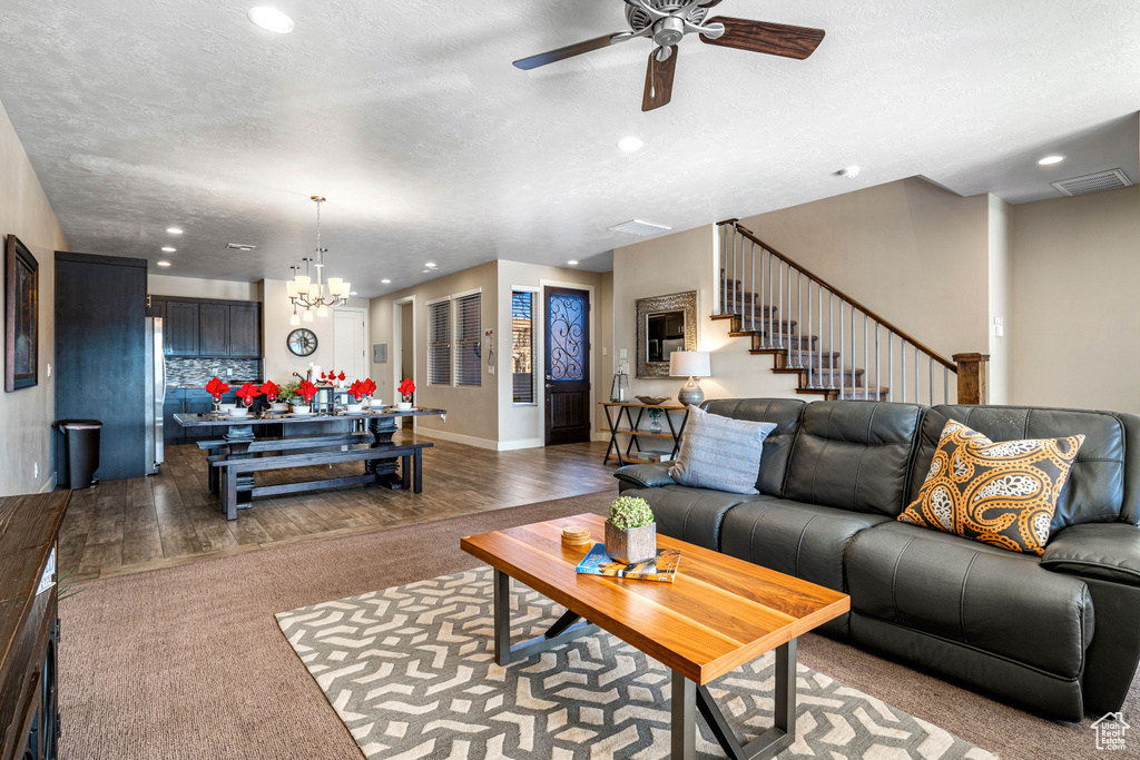 Living area with dark wood-type flooring, a ceiling fan, stairway, a chandelier, and recessed lighting