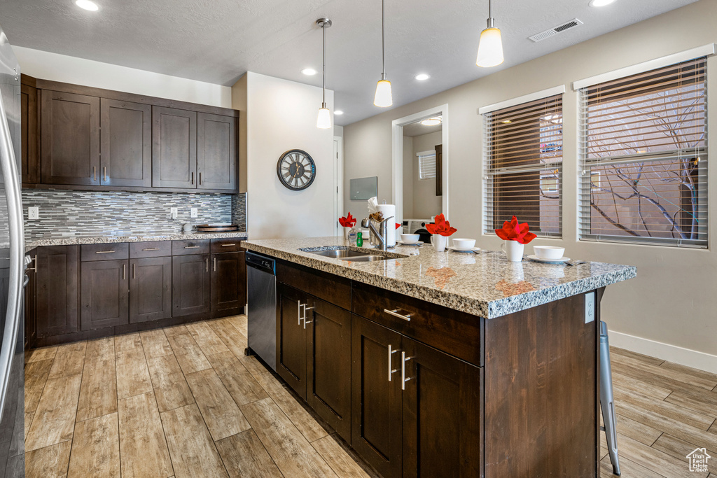 Kitchen featuring a sink, stainless steel dishwasher, light wood finished floors, tasteful backsplash, and light stone countertops