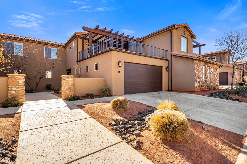 View of front of house featuring a balcony, stucco siding, a tiled roof, concrete driveway, and an attached garage