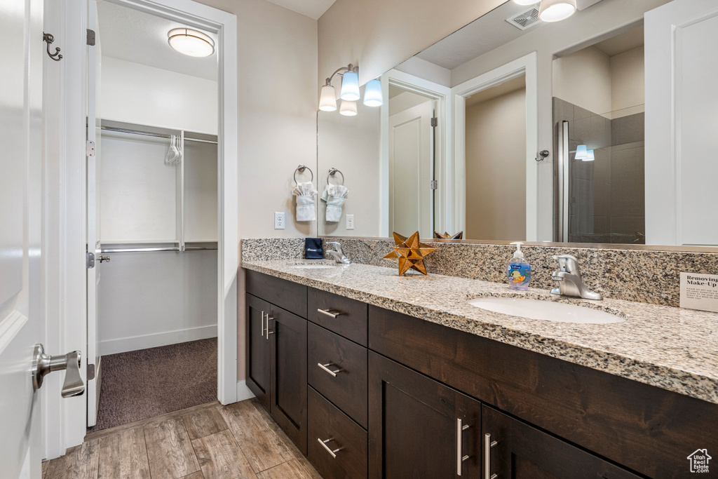 Full bathroom with a walk in closet, wood finished floors, double vanity, and tiled shower