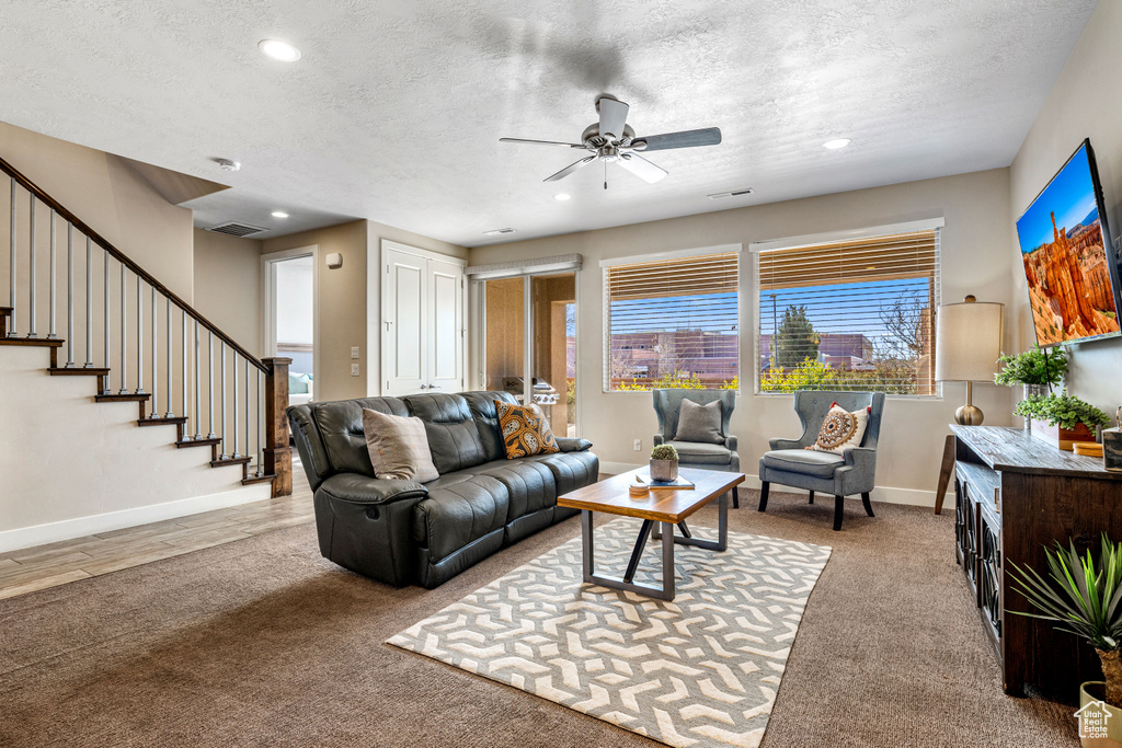 Living area with a ceiling fan, plenty of natural light, a textured ceiling, carpet flooring, and stairs