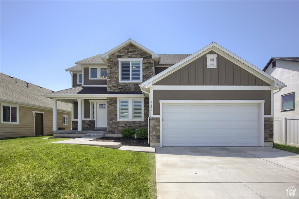 Craftsman house featuring stone siding, board and batten siding, a front yard, and concrete driveway