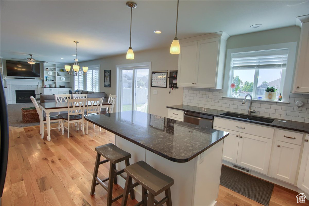 Kitchen featuring a sink, a fireplace, decorative backsplash, light wood-style flooring, and dishwasher