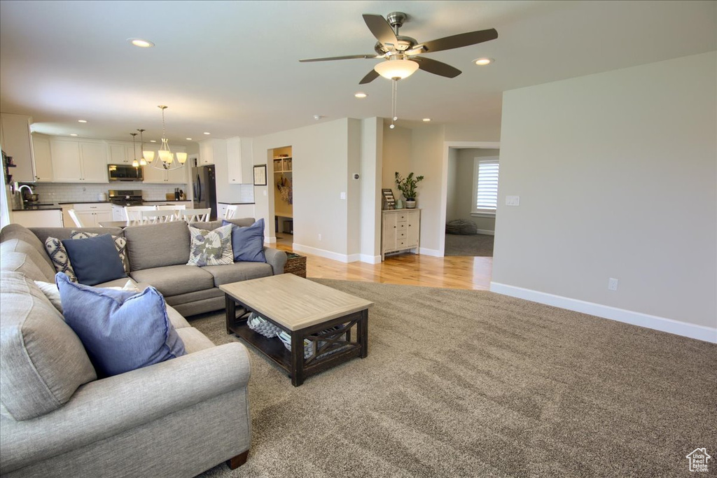 Living room featuring a ceiling fan, recessed lighting, baseboards, a chandelier, and light carpet