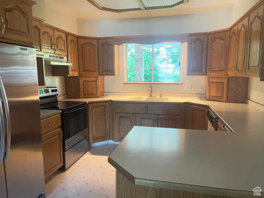 Kitchen with appliances with stainless steel finishes, a sink, under cabinet range hood, a peninsula, and light floors
