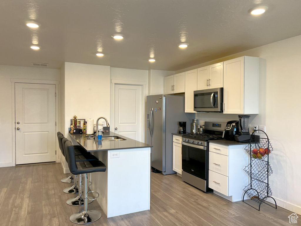 Kitchen with appliances with stainless steel finishes, a sink, dark countertops, a kitchen bar, and wood finished floors