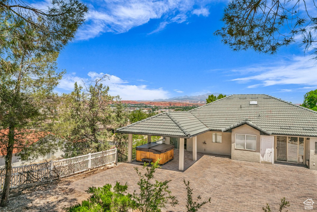 Back of house featuring a hot tub, a tile roof, stucco siding, a patio area, and a fenced backyard