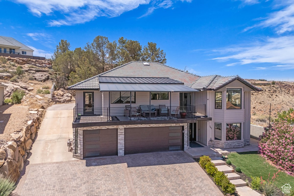 View of front facade featuring an attached garage, decorative driveway, a balcony, and stone siding