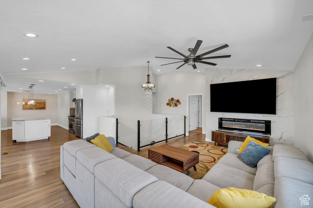 Living room with recessed lighting, a ceiling fan, light wood-type flooring, a fireplace, and vaulted ceiling