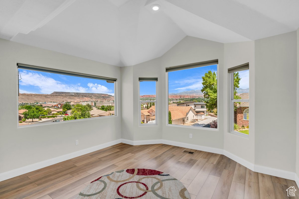 Unfurnished room with healthy amount of natural light, lofted ceiling, wood finished floors, and baseboards