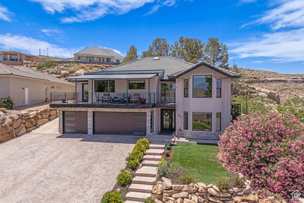 Contemporary home with a balcony, an attached garage, decorative driveway, and stone siding